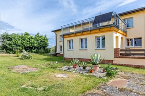 A two-story house with a balcony, a garden with potted plants, and a paved area.