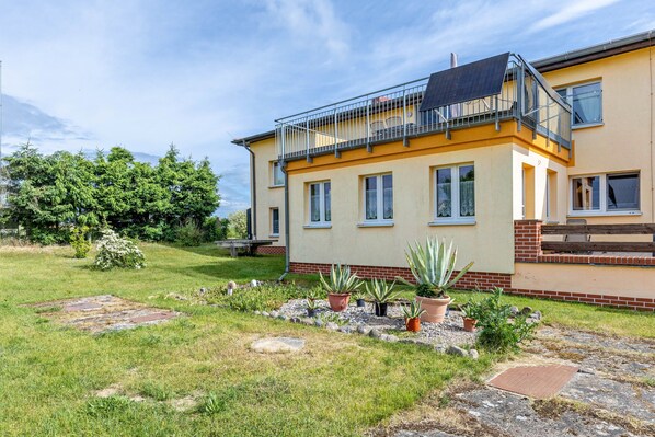 Une maison à deux étages avec un balcon, un jardin agrémenté de plantes en pot et une zone dallée.