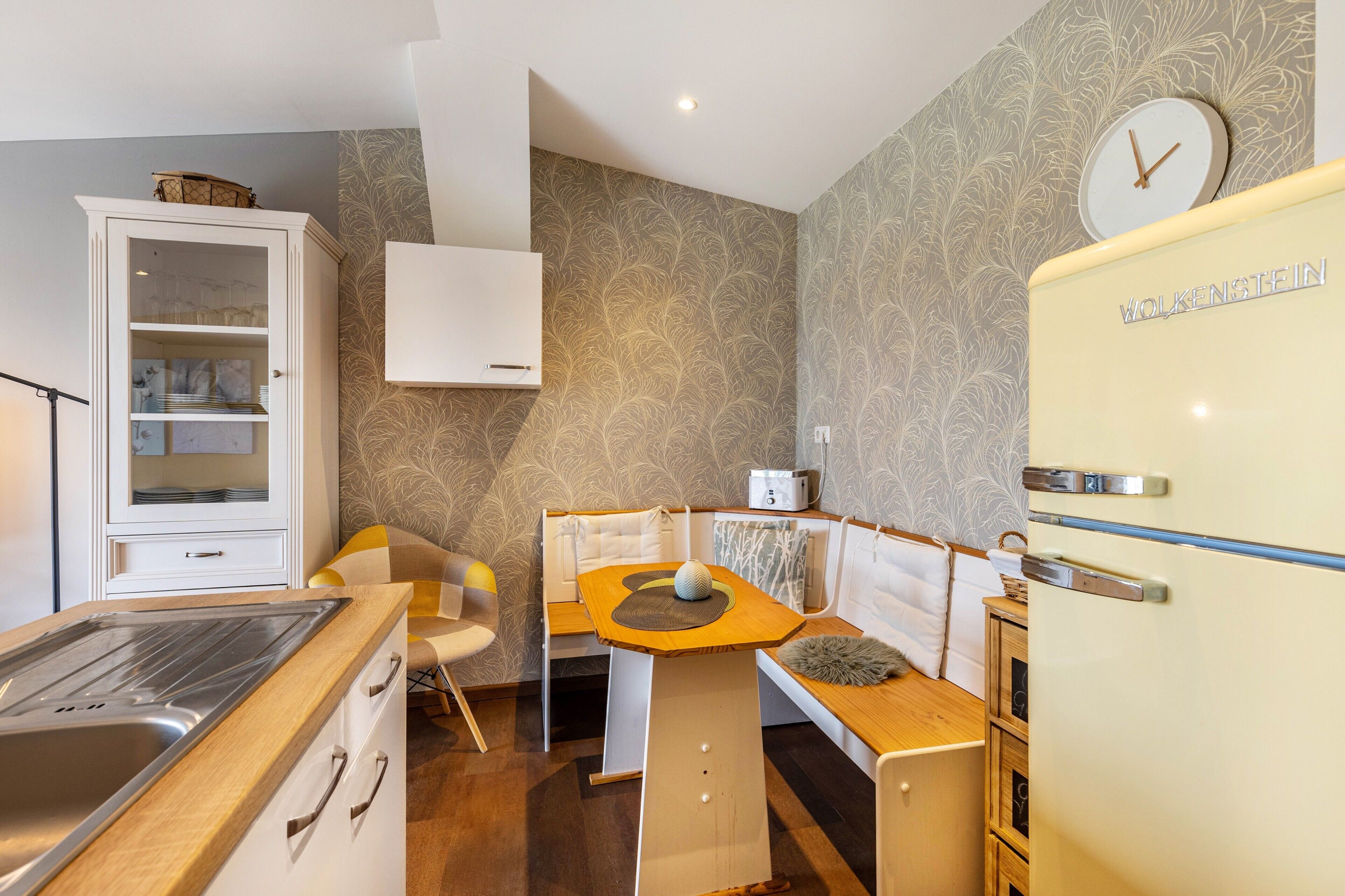 Cocina compacta con estufa integrada, refrigerador y comedor con banco y sillas.