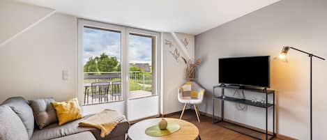 Una sala moderna con sofá, una mesa de centro, un televisor en un mueble bajo y un balcón con vistas.