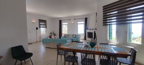 A spacious living area with a dining table, chairs, a sofa, and a fireplace. - Villa Margarita Batsi (Idrousa)