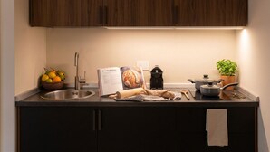 Een keuken met een spoelbak, een boek, een deegroller, een pan, een plant en een schaal met fruit.