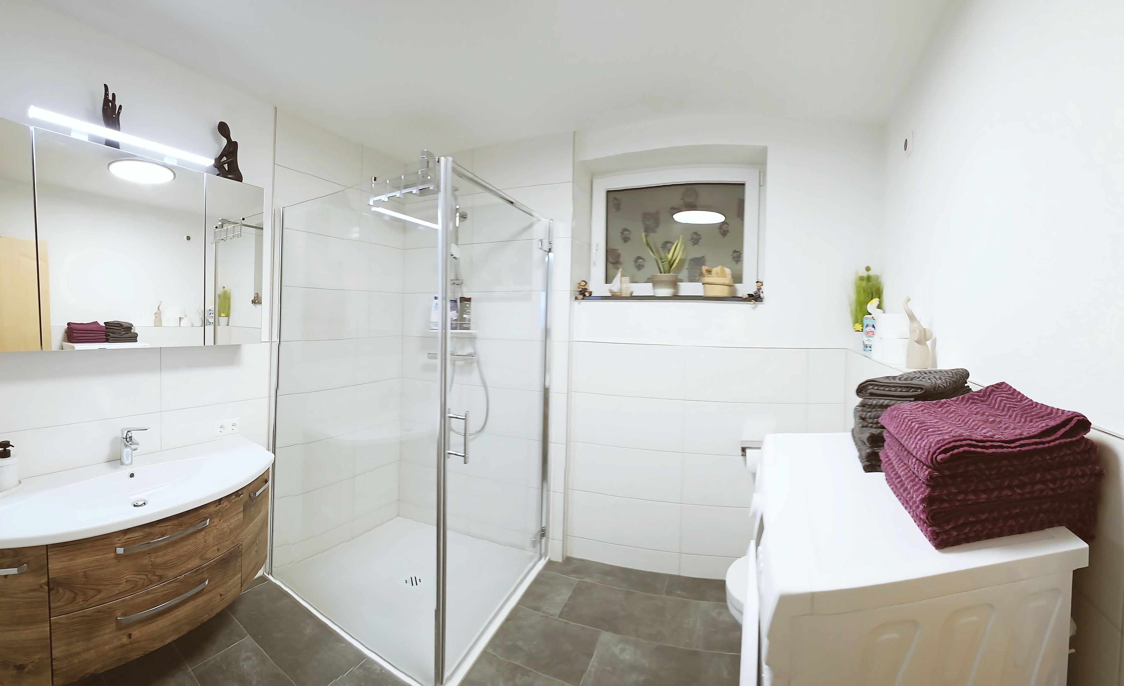 Ein modernes Badezimmer mit einer Duschkabine, einem weißen Waschtisch und einem kleinen Fenster.