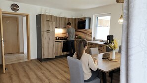 A modern kitchen with wooden cabinets, a microwave, and a person cooking. - Apartment 'Koni's Ferienwohnung' with Mountain View and Covered Parking Space (Rangersdorf)