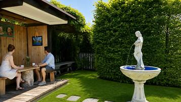 A wooden outdoor seating area with a fountain and a hedge in the background.