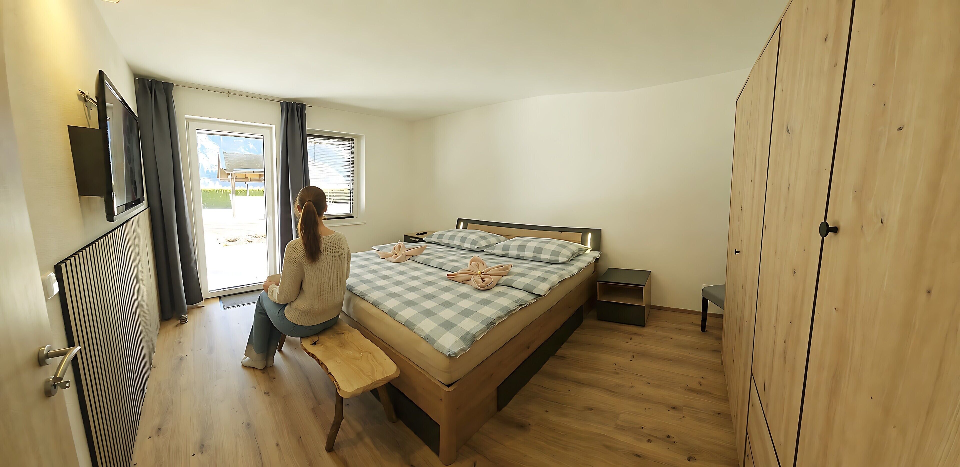 A bedroom with a bed, a bench, a bedside table, a wardrobe, and a window with curtains.