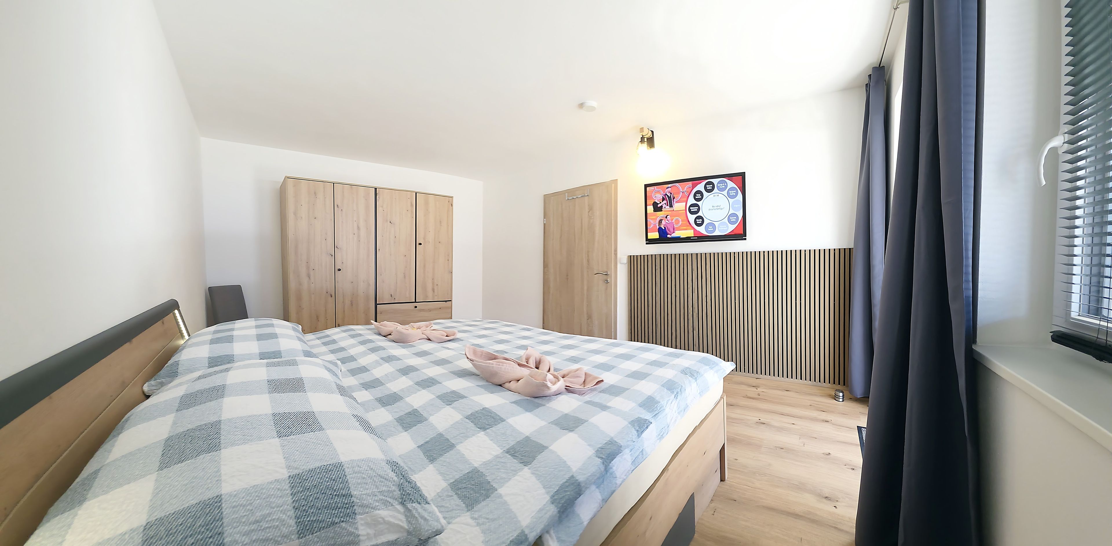 Un dormitorio con edredón a cuadros, armario de madera y televisor en la pared.