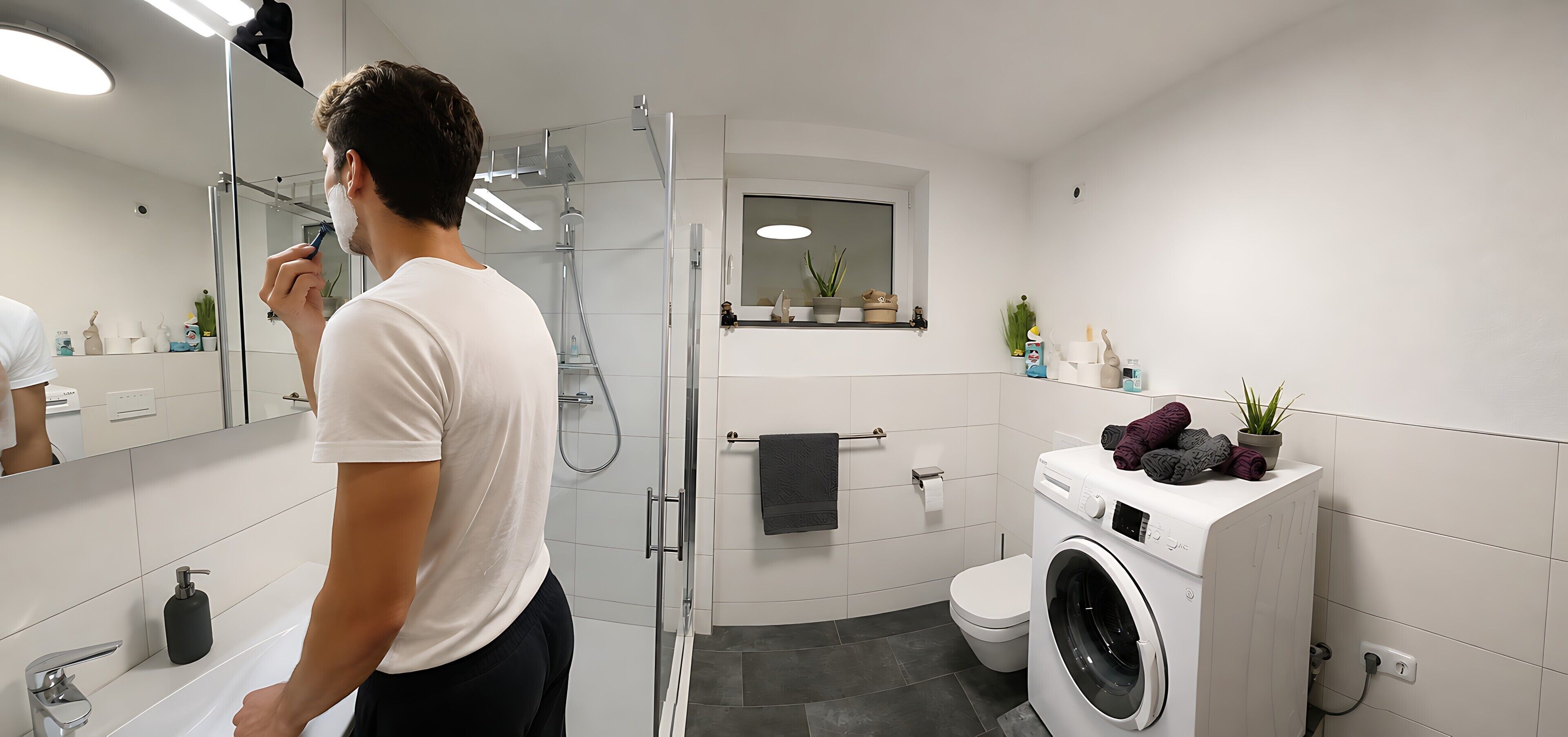 A modern bathroom with a glass shower enclosure, a white washing machine, and a mirror reflecting the room.