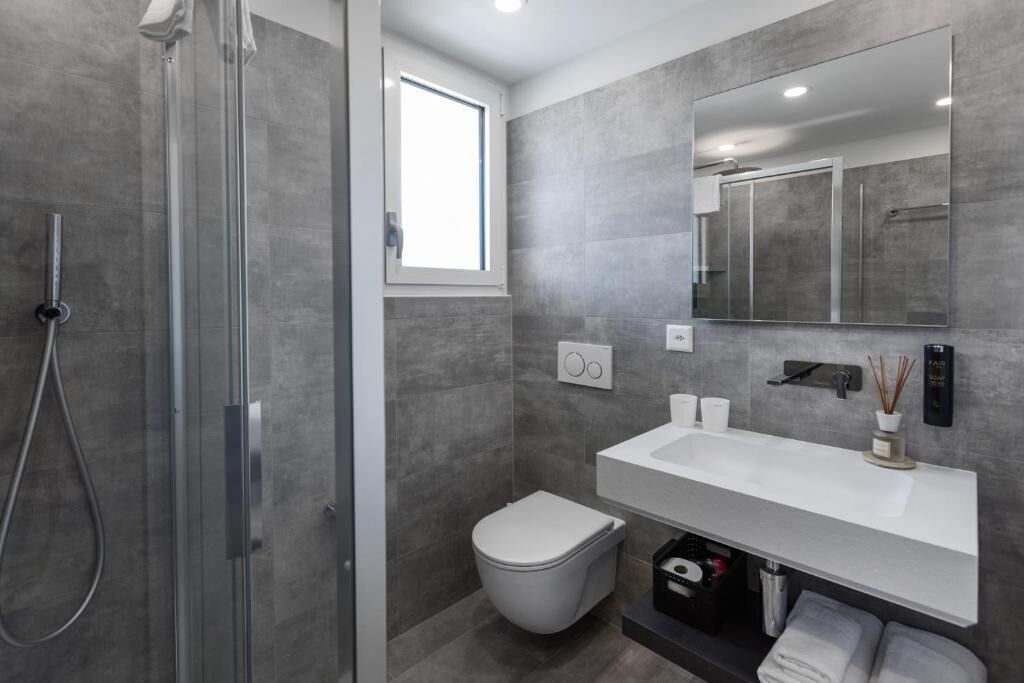 A modern bathroom with a glass shower enclosure, a white toilet, and a large mirror above a white sink.