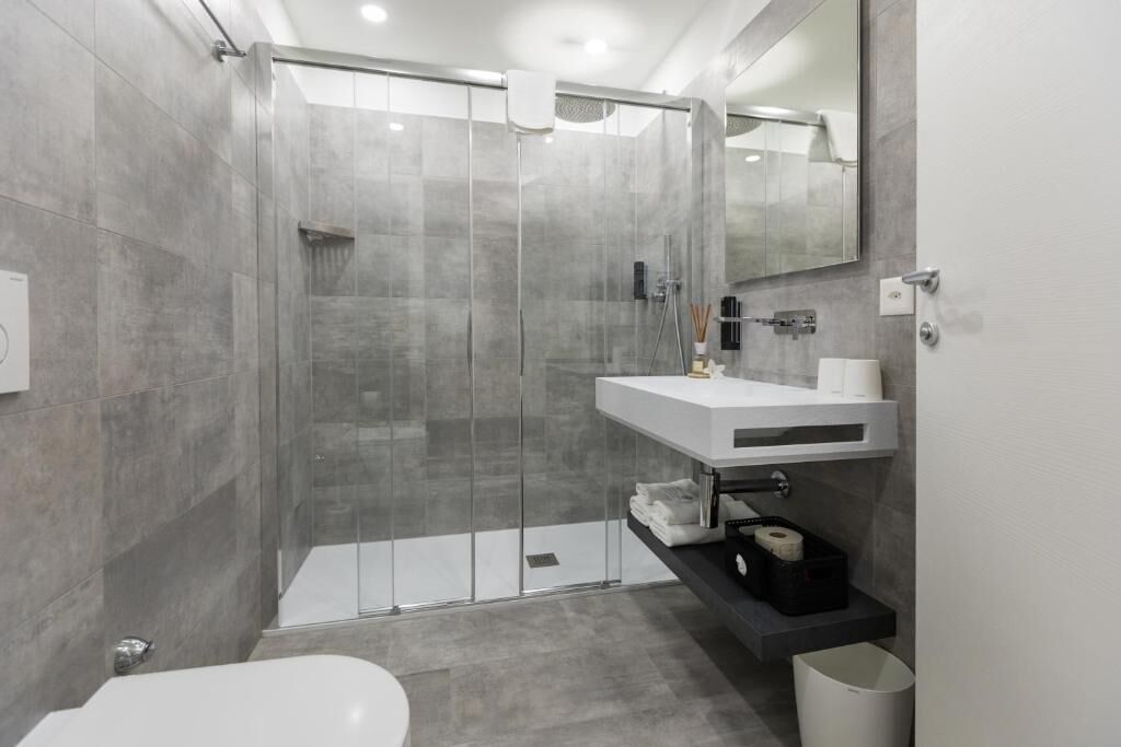 Ein modernes Badezimmer mit einer gläsernen Duschkabine, einem weißen Waschbecken und einer Toilette.