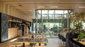 Ein modernes Restaurant mit Holzbalkendecke, Glaswänden und unterschiedlichen Sitzmöglichkeiten.
