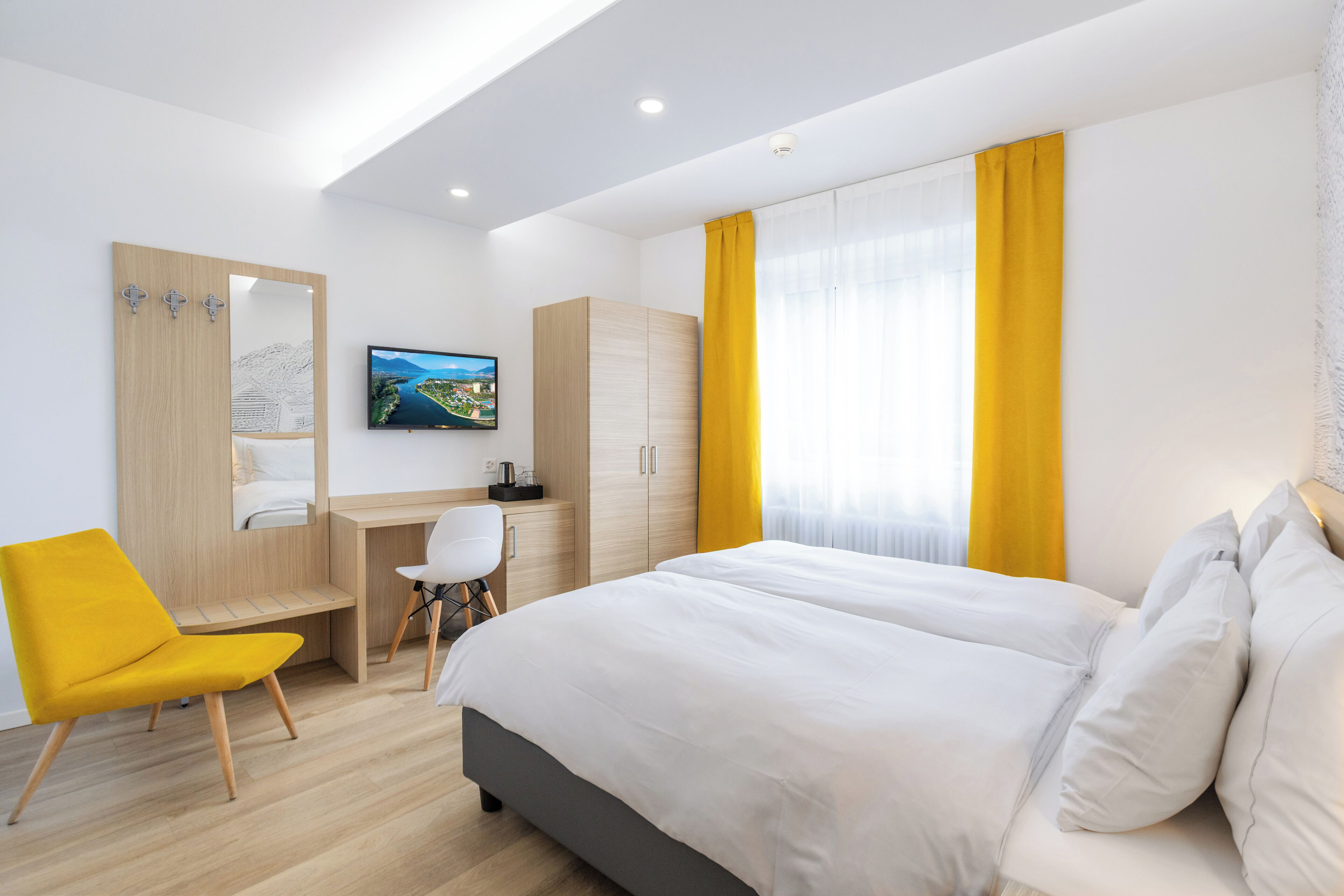 A modern hotel room with a large bed, a desk, a chair, and a wardrobe.
