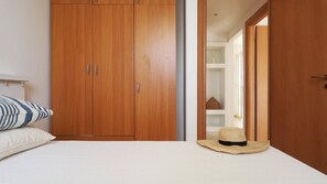 Un dormitorio con un armario de madera, una cama con ropa de cama blanca y un sombrero de paja en el suelo.