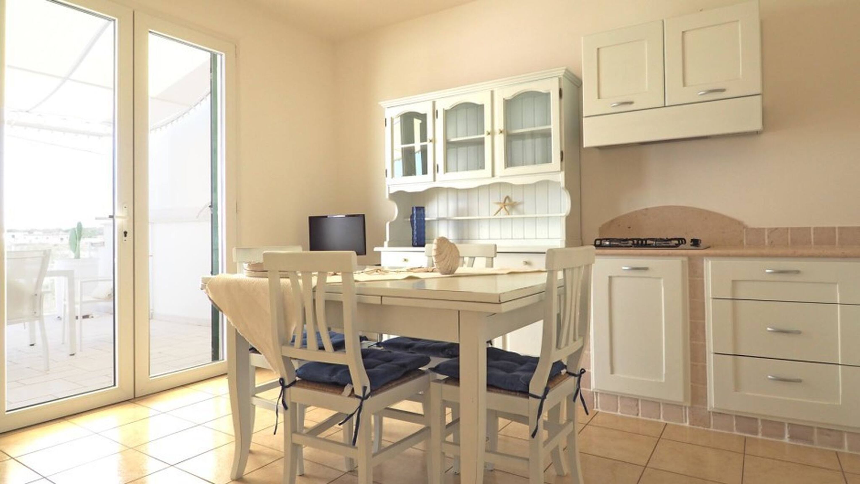 A kitchen with white cabinets, a dining table with chairs, and a sliding glass door leading to an outdoor area.