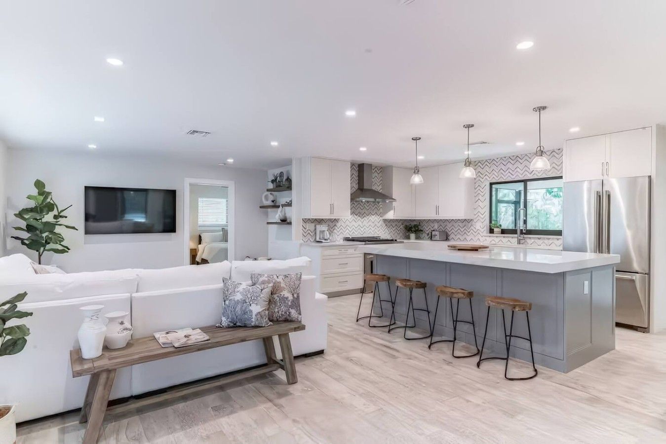 A modern kitchen with a central island, bar stools, and a dining area with a white sofa.