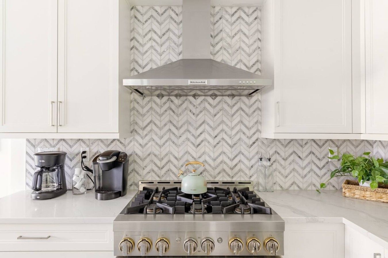 Une cuisine équipée d’une cuisinière à gaz, d’une machine à café, d’une bouilloire et d’un dosseret décoré d’un motif en chevrons.