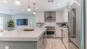 Cozinha moderna com uma bancada grande, eletrodomésticos de aço inoxidável e iluminação pendente.