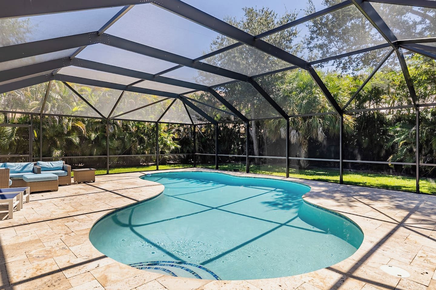 A covered swimming pool with a curved edge, surrounded by a patio area with outdoor furniture.