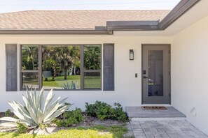 A modern house with a grey door, large windows, and a small garden with plants. - Stylish 3BR w/ Heated Pool · 7 Mins to Beach (Jupiter)