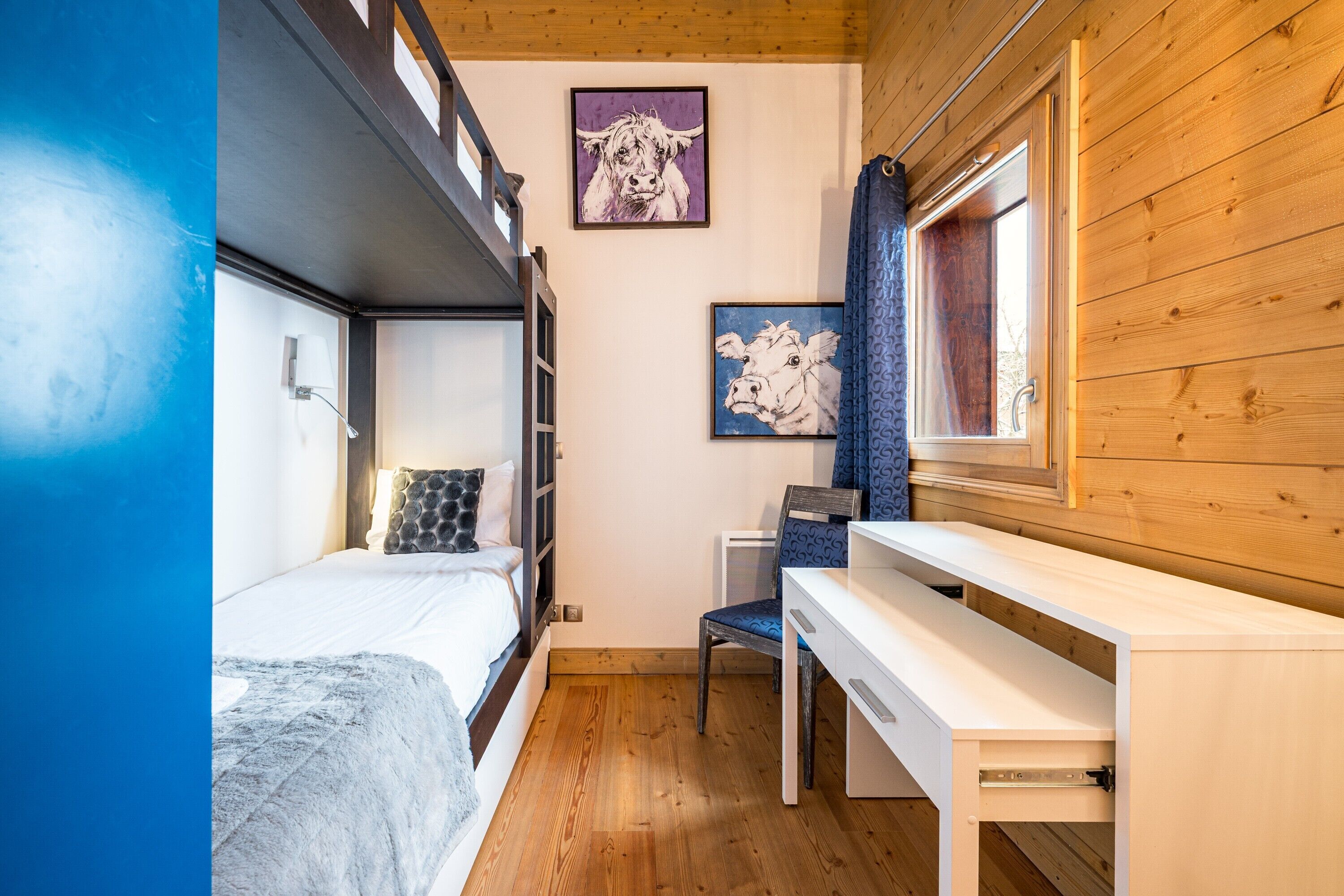 Une chambre avec un lit superposé, un bureau, une chaise et deux tableaux encadrés au mur.