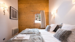 A bedroom with a wooden ceiling, a bed with white linens, a fluffy grey blanket, and a framed picture on the wall.