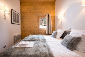 Une chambre avec un plafond en bois, un lit recouvert de draps blancs, une couverture grise et moelleuse, et un tableau encadré accroché au mur.