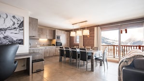 A modern kitchen with a dining area, large windows, and a view of mountains.