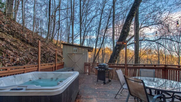Una terraza de madera con un jacuzzi, una parrilla y una mesa de vidrio con sillas.