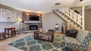 Una sala de estar con chimenea, una escalera y un sillón estampado.
