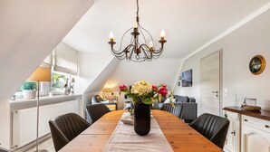 Ein Essbereich mit einem Holztisch, Stühlen, einer Blumenvase und einem Kronleuchter.