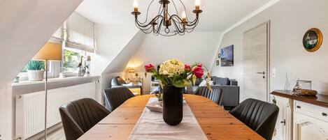A dining area with a wooden table, chairs, a vase with flowers, and a chandelier.