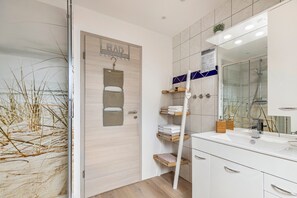 Une salle de bain moderne dotée d’une douche à parois de verre, d’une porte en bois avec un porte-serviettes et d’un meuble-lavabo agrémenté d’un grand miroir et d’un espace de rangement pour les serviettes.