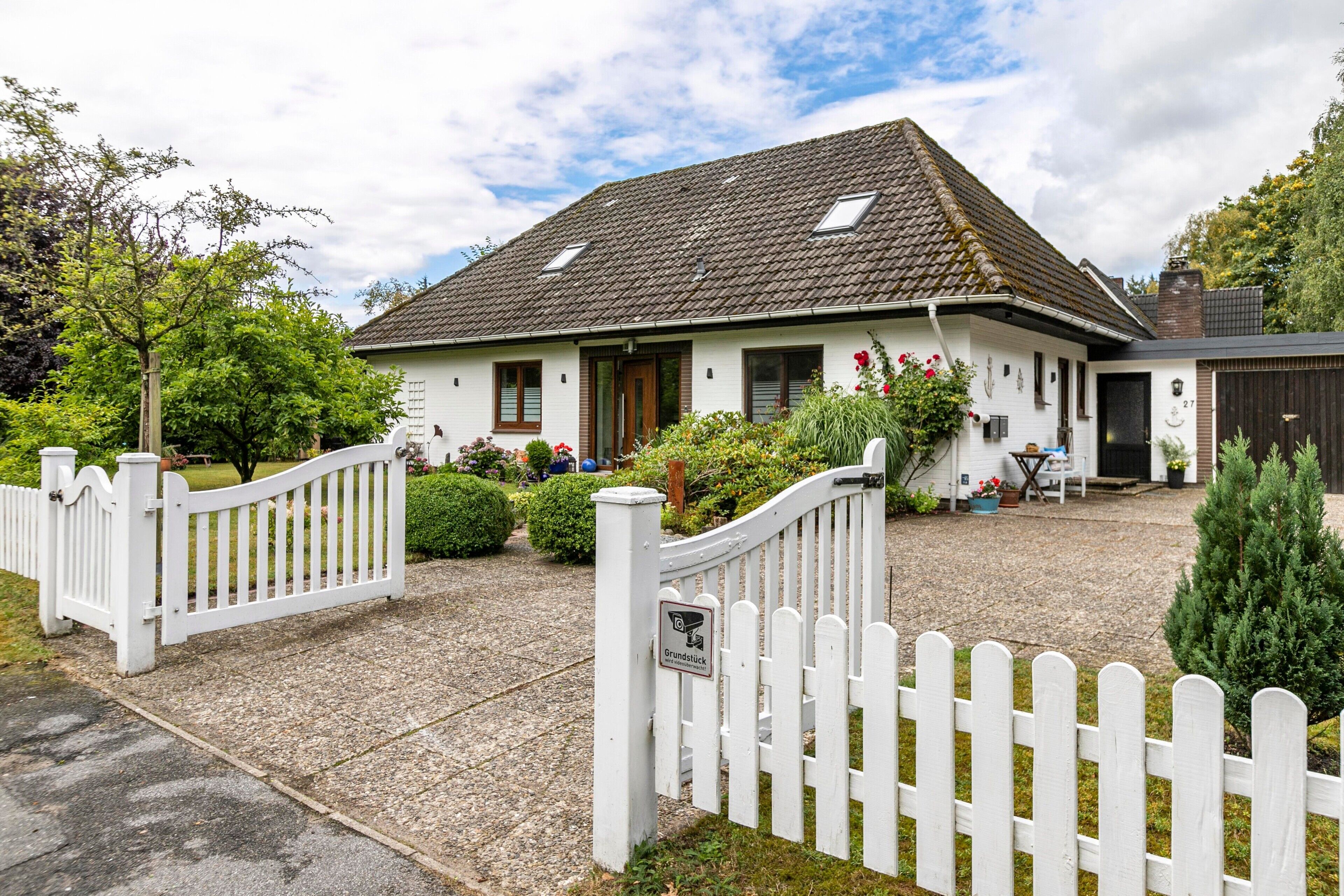 Une maison blanche avec un toit en tuiles, une clôture blanche en bois et une allée gravillonnée.