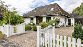 Une maison blanche avec un toit en tuiles, une clôture blanche en bois et une allée gravillonnée.