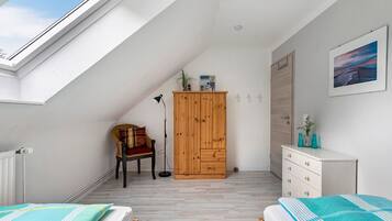 A bedroom with a skylight, a wooden wardrobe, a chair, a desk, and a bed with a striped pillow.