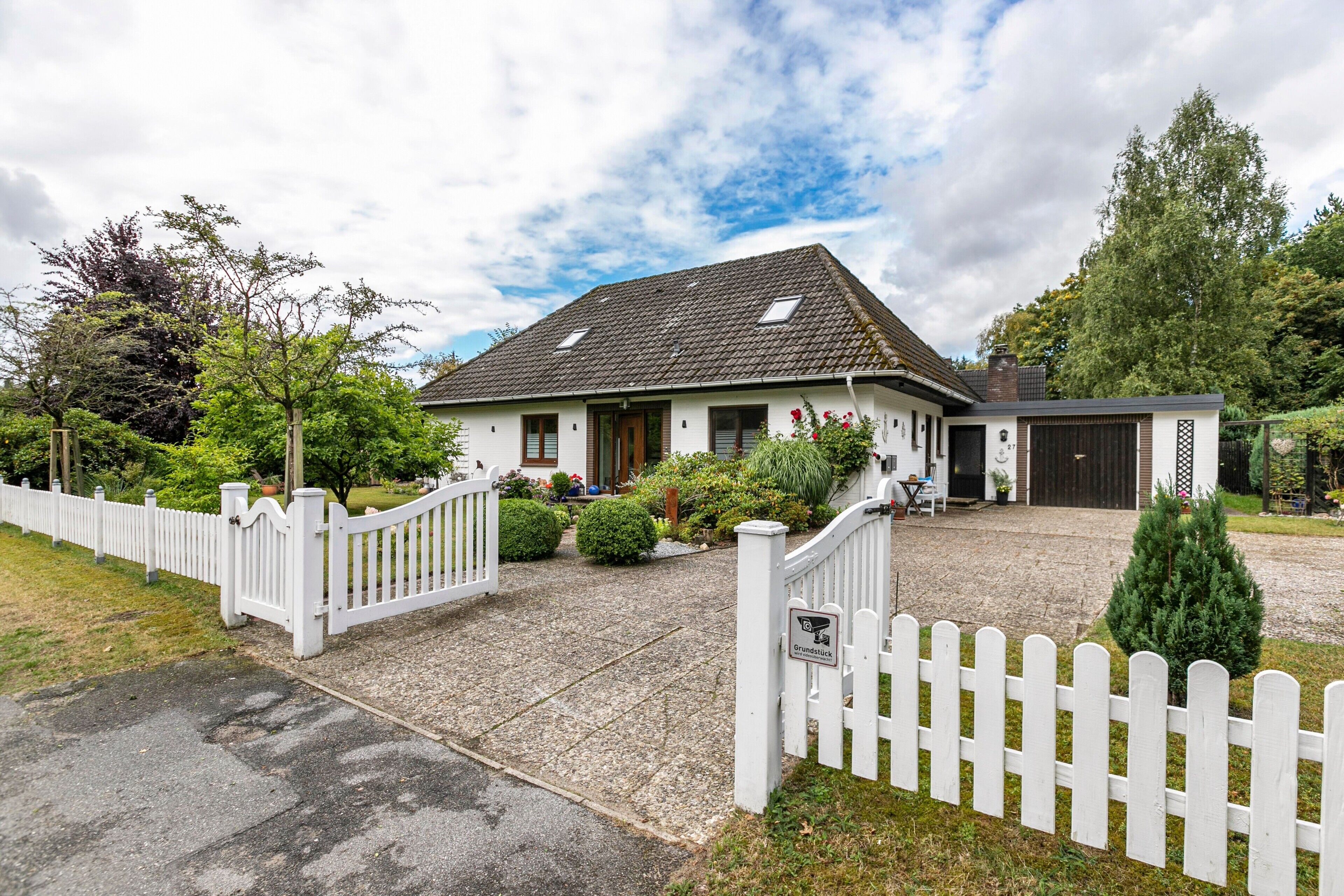 Une maison à deux étages, avec une façade blanche, un toit en pente et une allée gravillonnée.