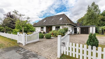Une maison à deux étages, avec une façade blanche, un toit en pente et une allée gravillonnée.