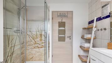 Ein modernes Badezimmer mit Duschkabine aus Glas, einer Holztür mit Handtuchhalter und einem Waschtisch ebenfalls mit Handtuchhalter.