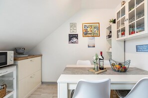 Una cocina moderna con muebles blancos, un microondas, una mesa de comedor con sillas y un armario de vidrio con vajilla.