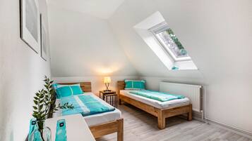 Een slaapkamer met twee bedden, een dakraam, een nachtkastje met een lamp en een plant.