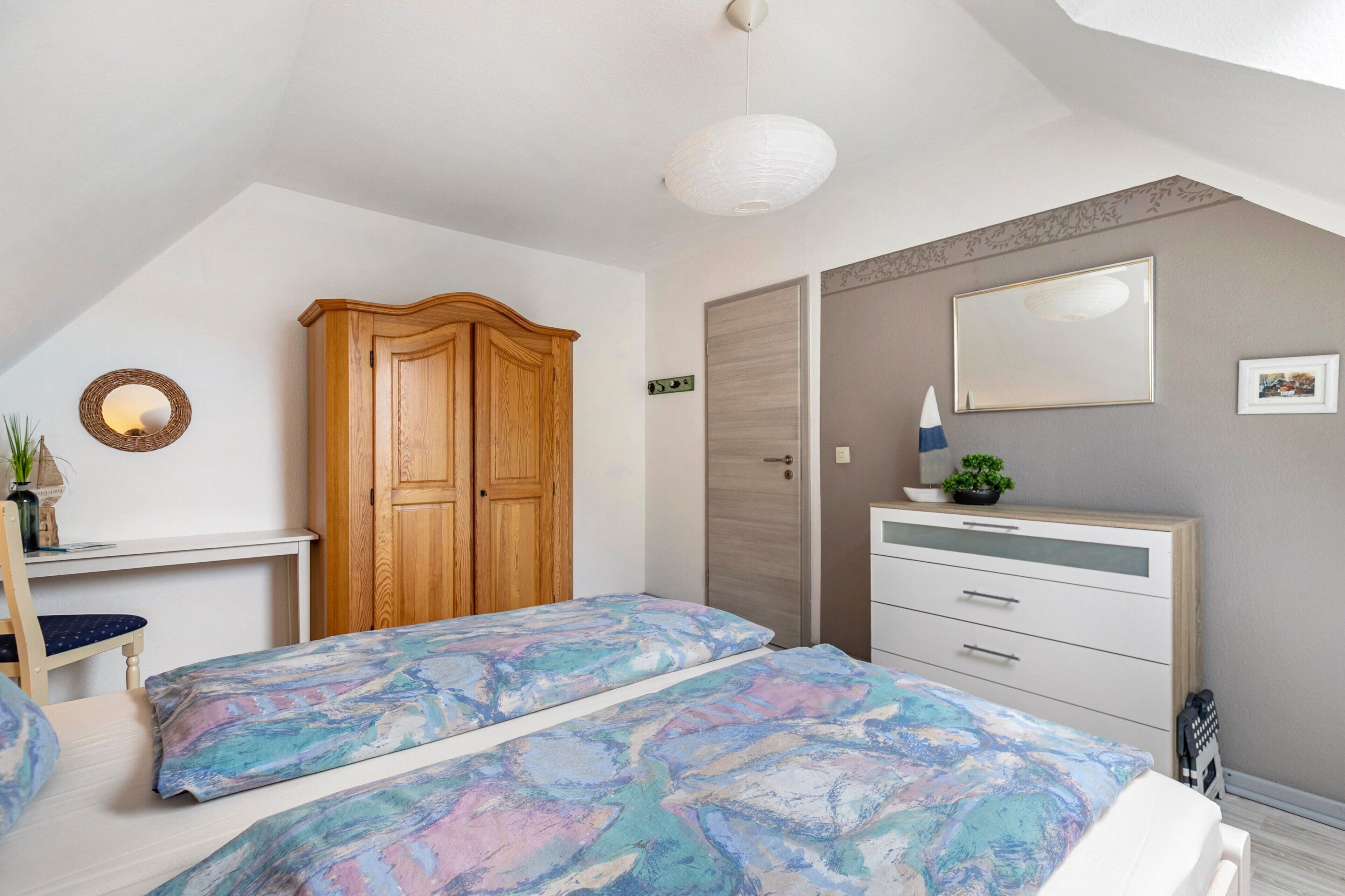 Un dormitorio con dos camas, un armario, una cómoda, un espejo y una lámpara colgante.