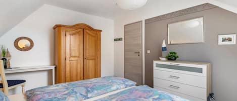 Quarto com duas camas, guarda-roupa, penteadeira, espelho e luminária suspensa.