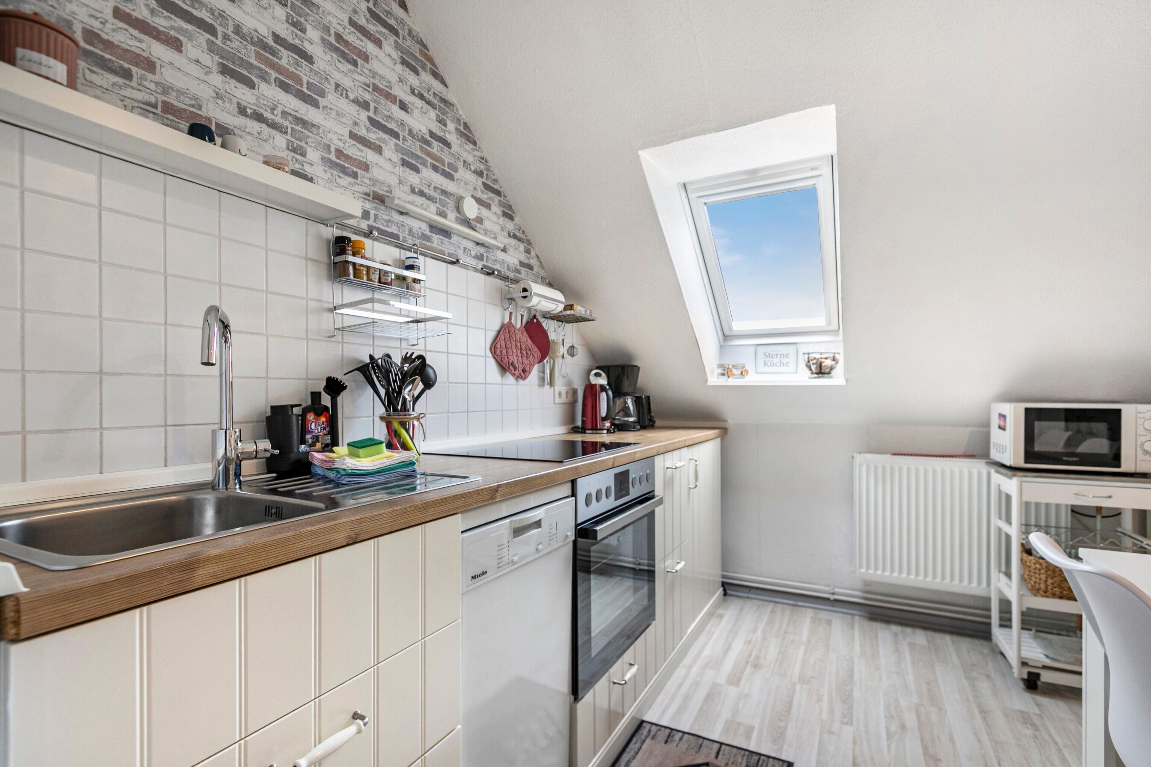 Una cocina moderna con pared de ladrillo, muebles blancos y ventana sobre el fregadero.