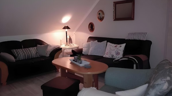 Un salon avec un canapé, une table basse et une lampe. On y trouve des coussins décoratifs et des œuvres d’art murales.