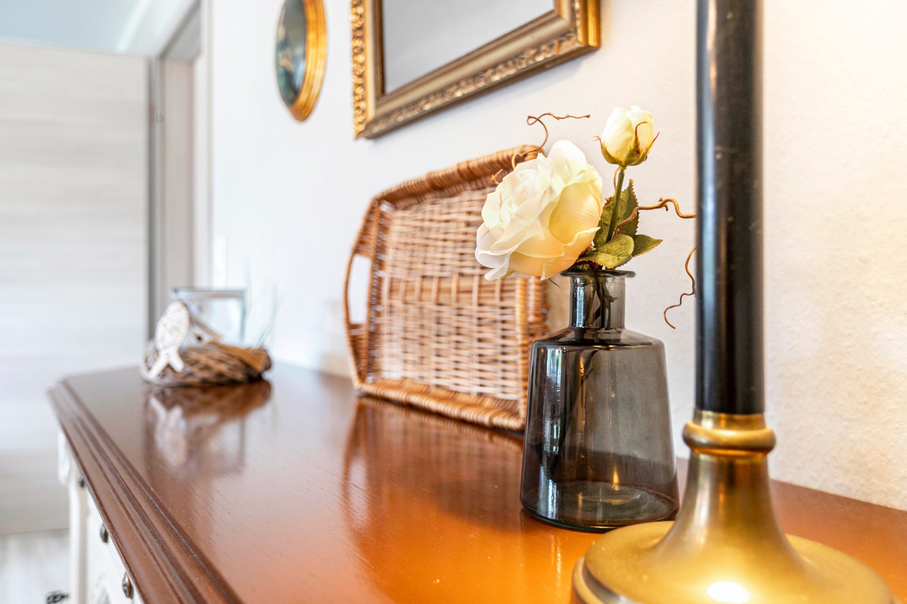 Une table en bois sur laquelle se trouvent un vase de roses blanches, une bouteille en verre et un panier en osier.