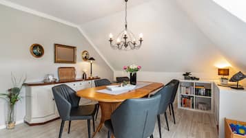 Un coin repas avec une table en bois, des chaises à revêtement gris, un lustre et une bibliothèque.