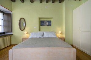 A bedroom with a bed, two bedside lamps, a mirror, a picture on the wall, and a wardrobe.