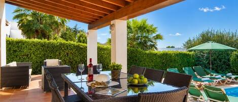 Un patio al aire libre con una mesa, sillas, una piscina y sillones de descanso.