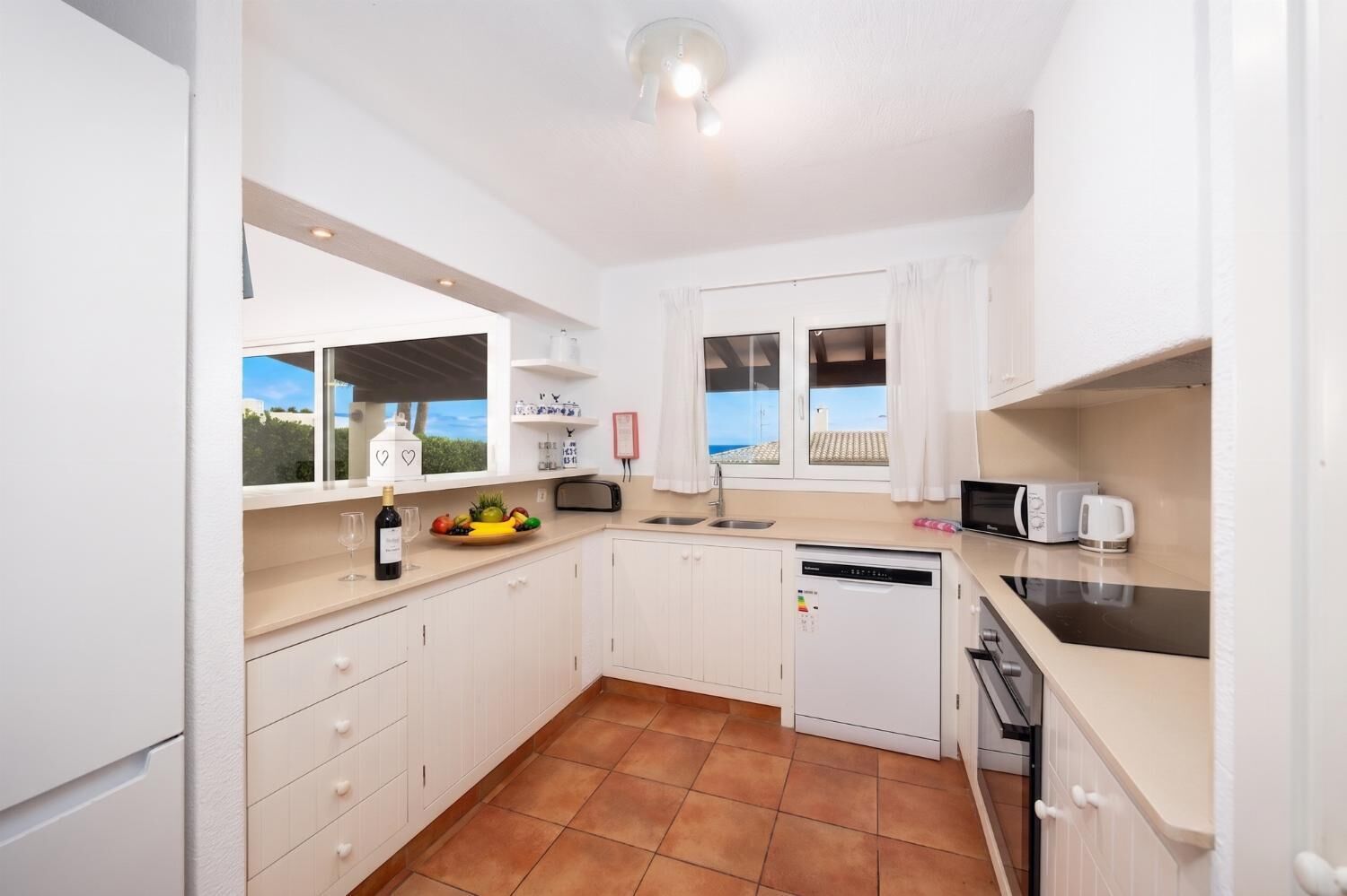 A compact kitchen with white cabinets, a dishwasher, a sink, and a window with a view.