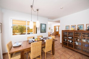 A dining area with a wooden table, wicker chairs, and a glass cabinet with dishes. - Villa Sa Calma - Four Bedroom Villa, Sleeps 8 (Puerto Luz)